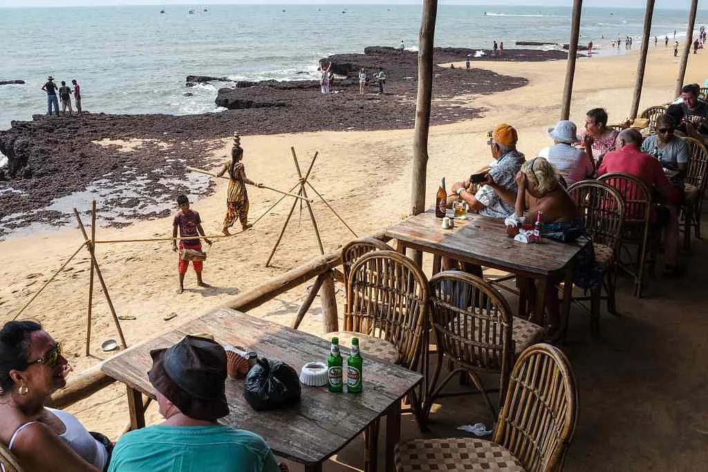 Tourists and visitors sit in a restaurant as children perform at Anjuna beach in Anjuna, Goa.