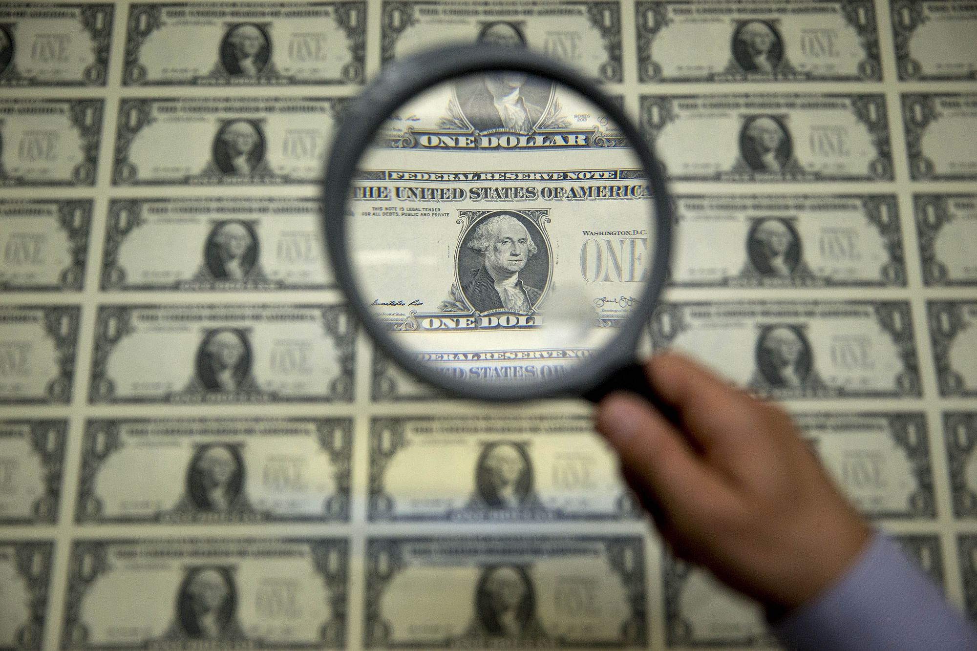 A magnifying glass is held over a one dollar note sheet in Washington, DC, US