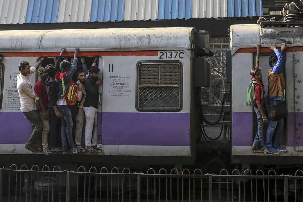 Passengers stand in the doorway, left, and on the side of train carriages as they travel by rail in Mumbai.
