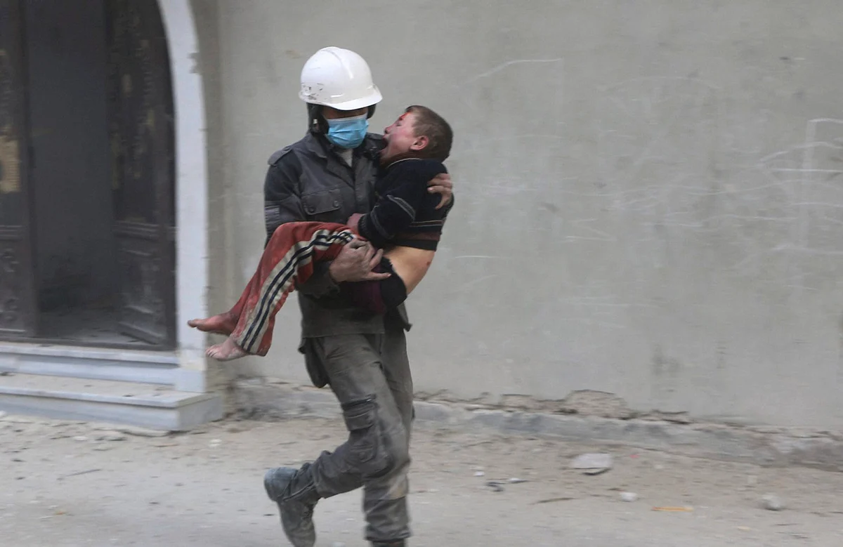 A member of Syrian Civil Defense group, the White Helmets, carries a boy who was wounded during airstrikes and shelling by Syrian government forces, in Ghouta, Syria. 