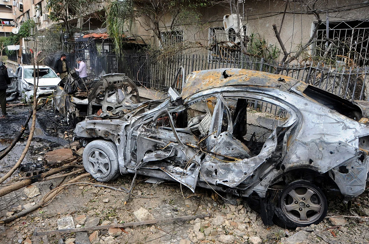 Syrians gather next to a burnt car hit by shells, at a highway in Damascus, Syria.