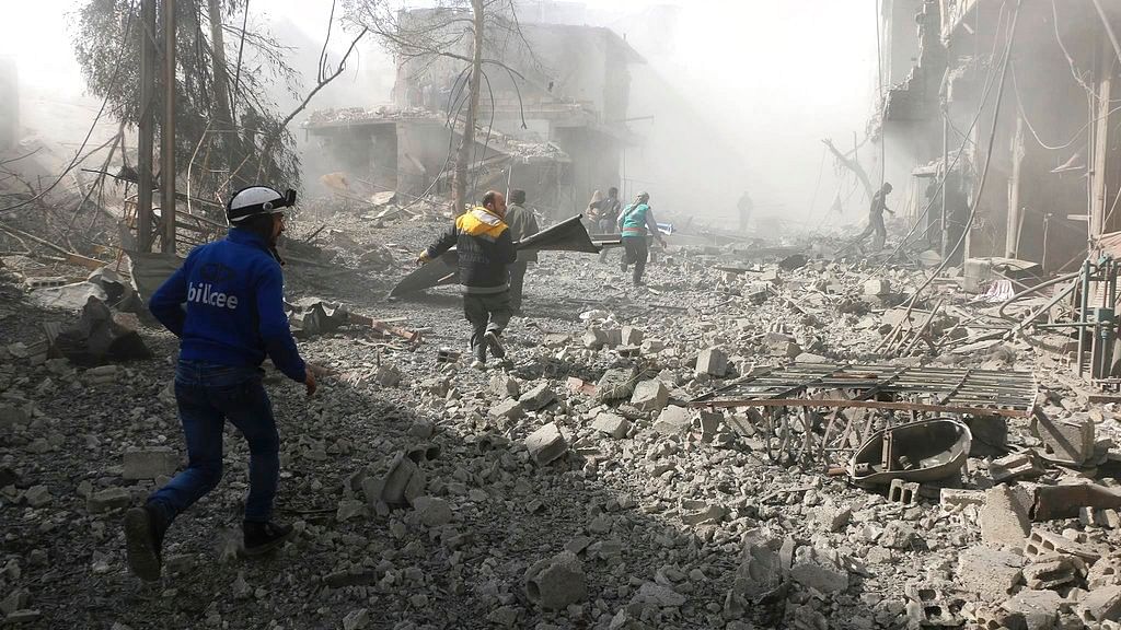 In this photo provided by the Syrian Civil Defense group known as the White Helmets, shows members of the Syrian Civil Defense run to help survivors from a street that attacked by airstrikes and shelling of the Syrian government forces, in Ghouta suburb of Damascus, Syria.