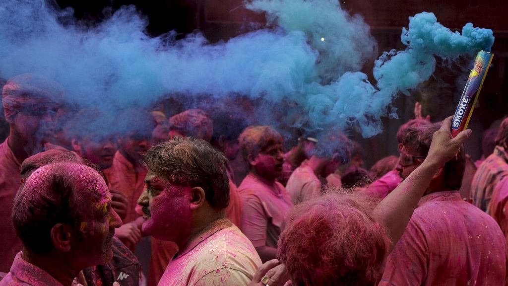 Locals light up a color smoke candle as a procession of  Krishna’s chariot moves through a street during Holi in Kolkata.
