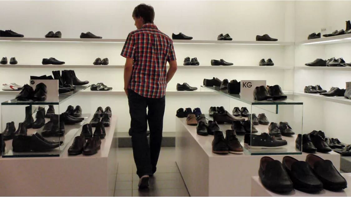 A man browsing the shoe department in a shopping centre. Cn he really afford new shoes?