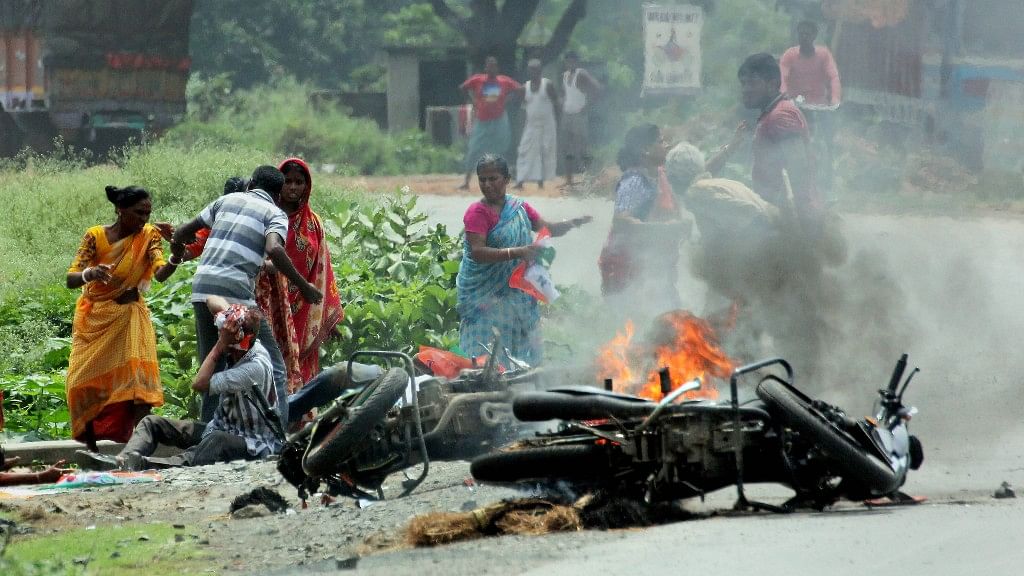 People injured in poll violence,  sit by the side of a road as a vehicle is set on fire by locals during Panchayat polls in  West Bengal