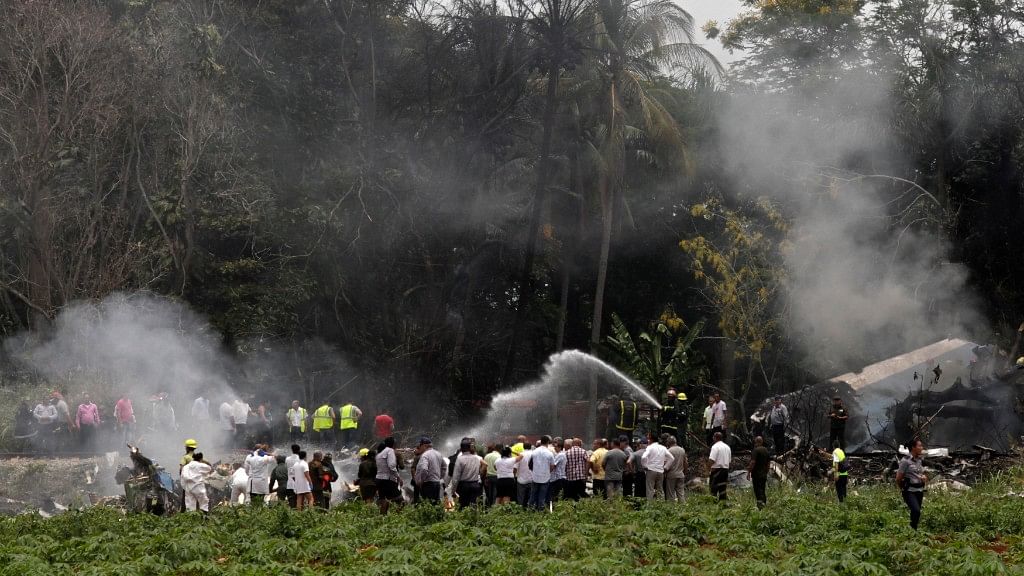 People look from afar at the remains of a Boeing 737 that plummeted into a yuca field with more than 100 passengers on board, in Havana, Cuba, Friday, 18 May.