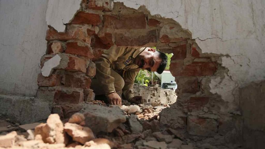 An Indian policeman looks at a hole made in a wall of a police station caused by a mortar shell.
