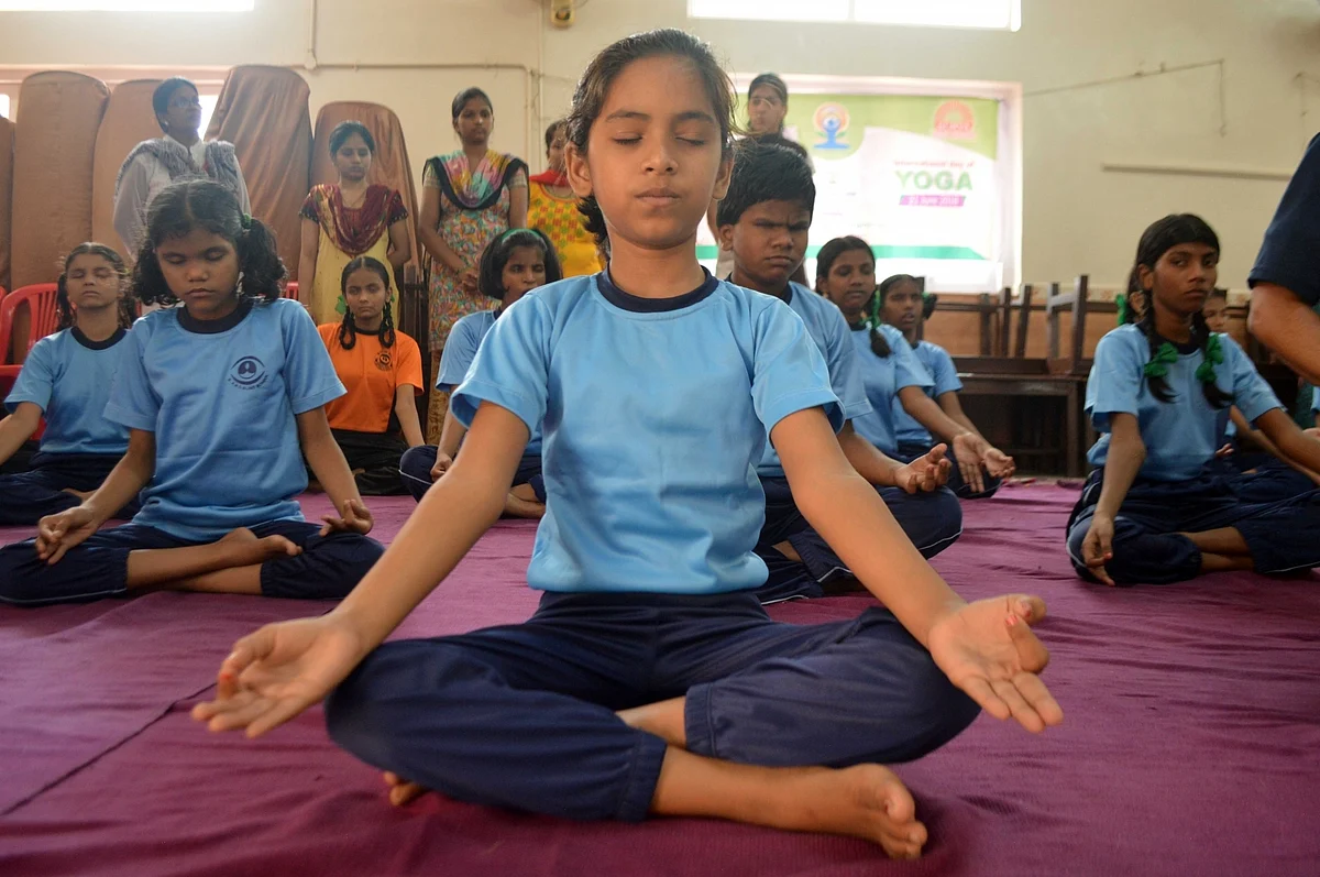 Visually-challenged students perform yoga in a school classroom.