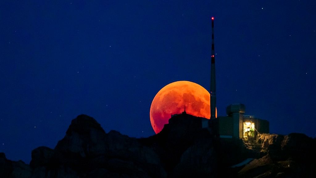 The moon turns red during a total lunar eclipse, behind the Saentis in Luzern, Switzerland, on Friday, 27 July.&nbsp;
