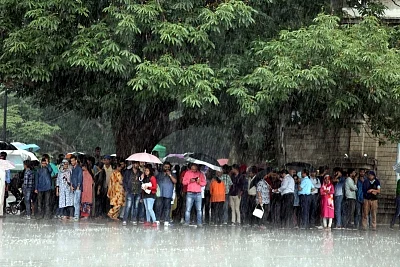 Shimla: People take shade under a tree as rain lashes Shimla. (Photo: IANS)