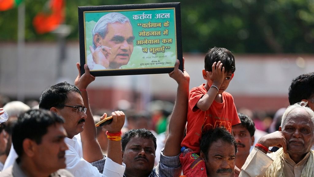 A mourner holds a portrait of former Indian Prime Minister Atal Bihari Vajpayee as he stands with others outside the BJP headquarters on 17 August.