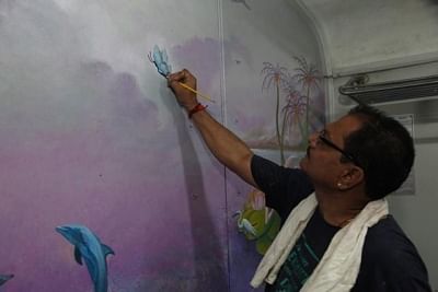 Mumbai: An artist busy painting the interiors of a ladies coach of a suburban train, in Mumbai on Sept 26, 2018. In an effort to provide a pleasing ride to women commuters, the Western Railway has painted the interiors of two ladies coaches of suburban trains with eye-catching scenic views, an official spokesperson said here on Wednesday. The painting shows birds singing on trees, dolphins jumping out of the water, a tiny land mass with coconut trees, lush greenery and flowery bushes. (Photo: IA