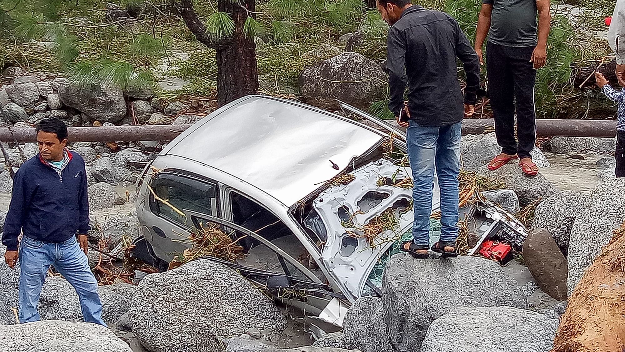 Locals inspect a damaged car washed ashore due to incessant rains, at Palampur.