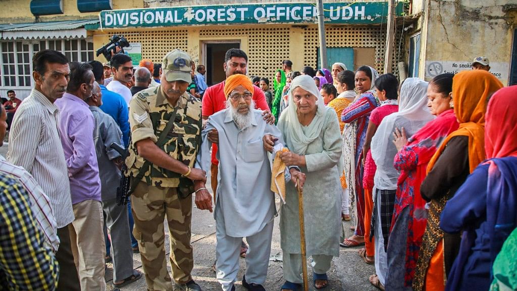 An elderly voter is assisted as he comes out after casting vote for the second phase of polling for municipal corporation elections, in Udhampur district, Jammu. 