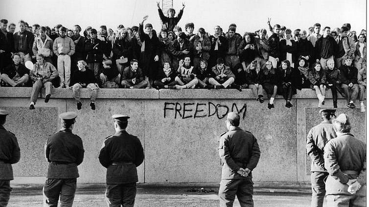File image of East German students sitting on the Berlin Wall in front of border guards.