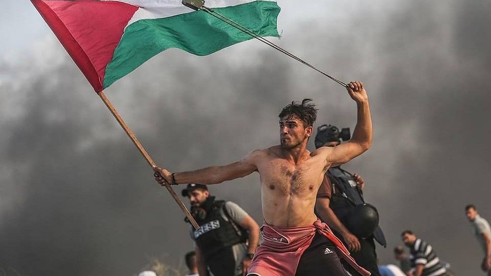 A photograph of 20 year-old A’ed Abu Amro with a slingshot in one hand and a Palestinian flag on the other went viral across social media.