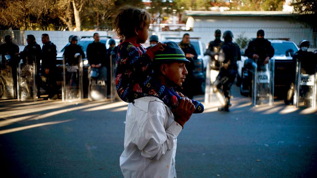A migrant carries a child past Mexican police who stand guard outside the Benito Juarez Sports Center which is serving as a shelter for migrants in Tijuana, Mexico. &nbsp;