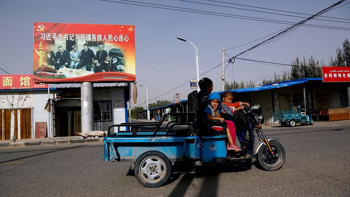 An Uighur woman shuttles school children on an electric scooter as they ride past a propaganda poster showing China’s President Xi Jinping joining hands with a group of Uighur elders in Hotan, in western China’s Xinjiang region.&nbsp;