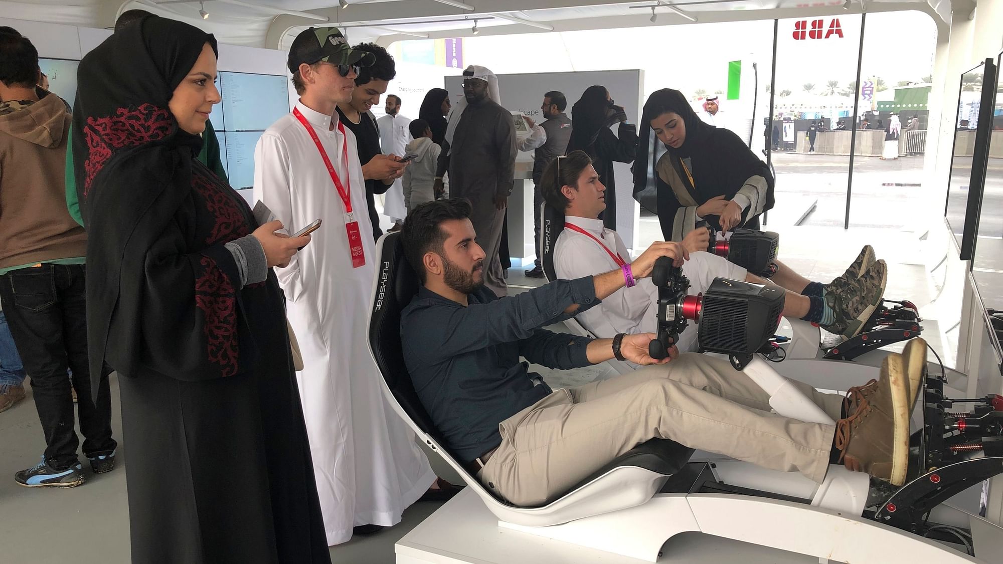 Hostesses in black robes and headscarves give instructions to foreign visitors trying out a simulator at a Formula-E race on the outskirts of Riyadh in Saudi Arabia.