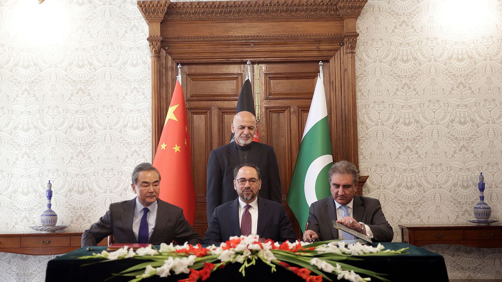 Afghanistan’s President Ashraf Ghani, standing, watches as Afghanistan’s Minister of Foreign Affairs Salahuddin Rabbani, center, Pakistan’s Foreign Minister Shah Mehmood Qureshi, right, and Chinese Foreign Minister Wang Yi, left, sign the agreement during the meeting.