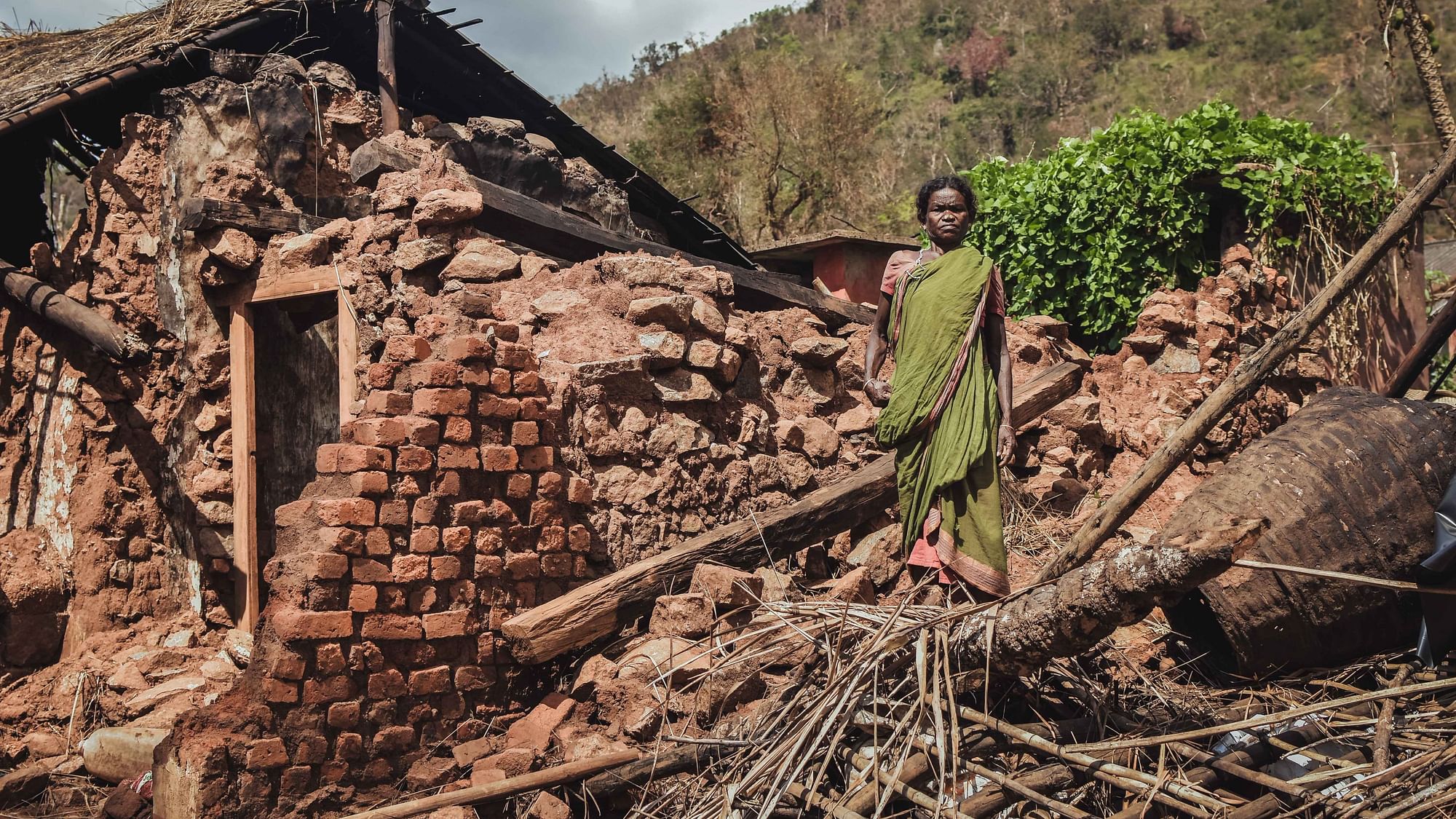 A woman stands in front of her broken house.&nbsp;