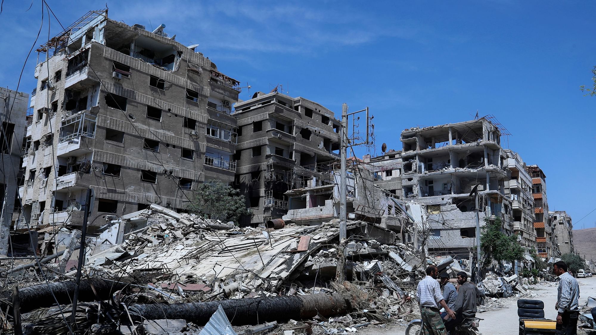 In this 16 April 2018 file photo, people stand in front of damaged buildings, in the town of Douma, the site of a suspected chemical weapons attack, near Damascus, Syria.