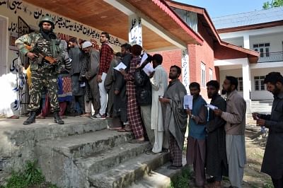 Kulgam: A security personnel stands guard as voters queue up to cast their votes for the fourth phase of 2019 Lok Sabha elections, at a polling station in Jammu and Kashmir