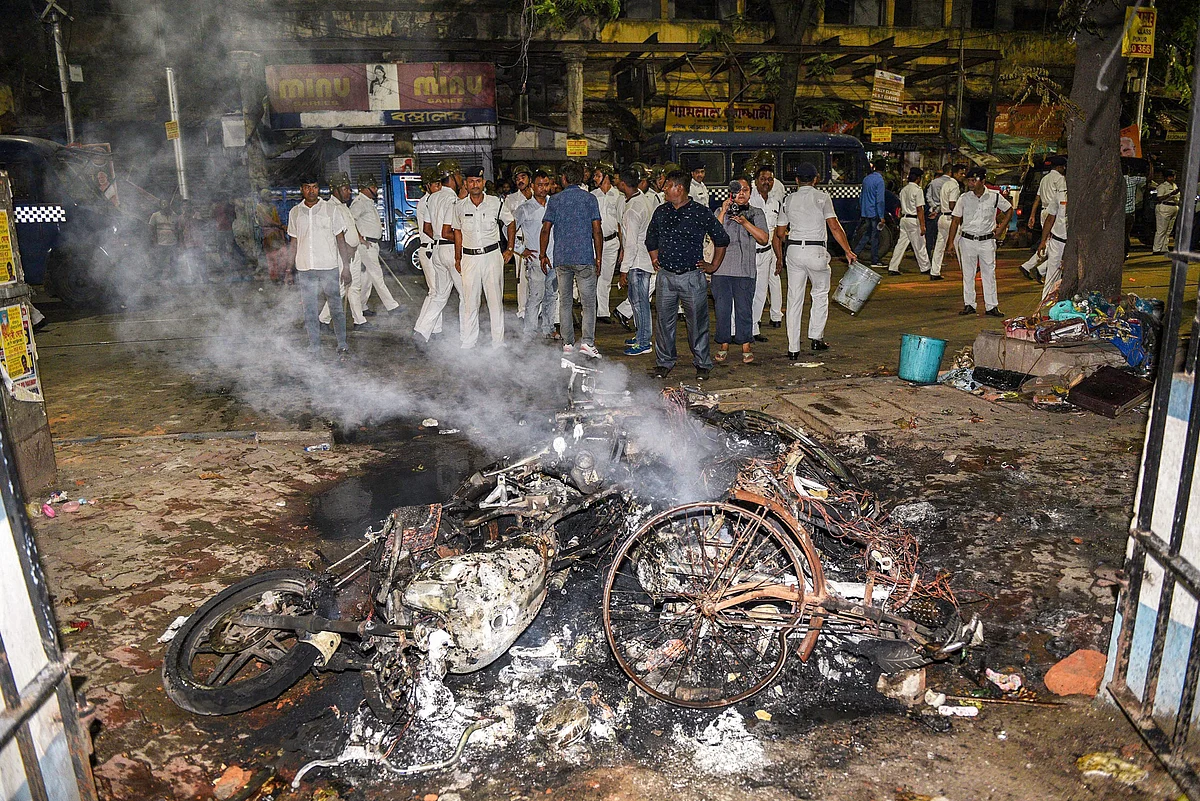 Police personnel look on near vehicles burnt by a mob during BJP President Amit Shah’s election roadshow.