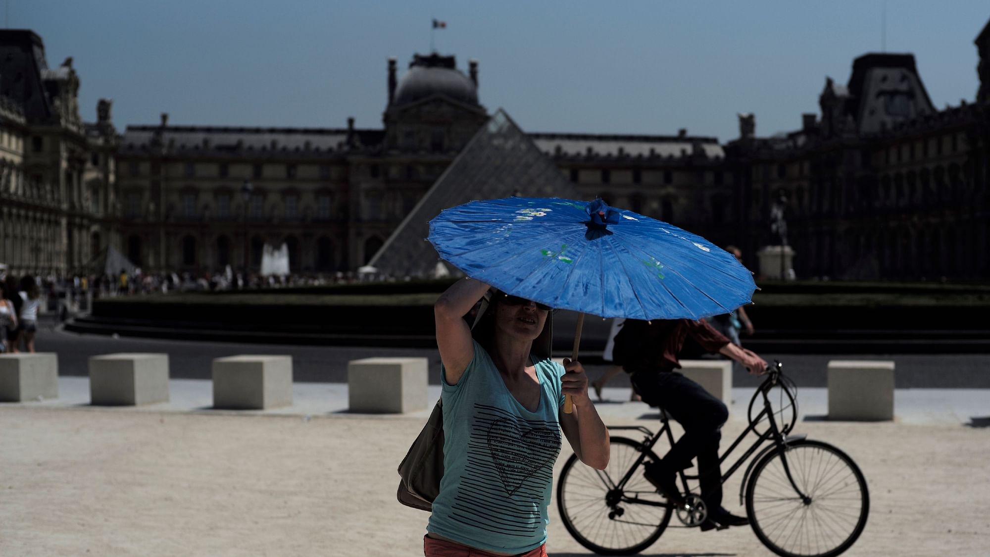 A woman holds a sunshade outside the Louvre Museum in Paris. 