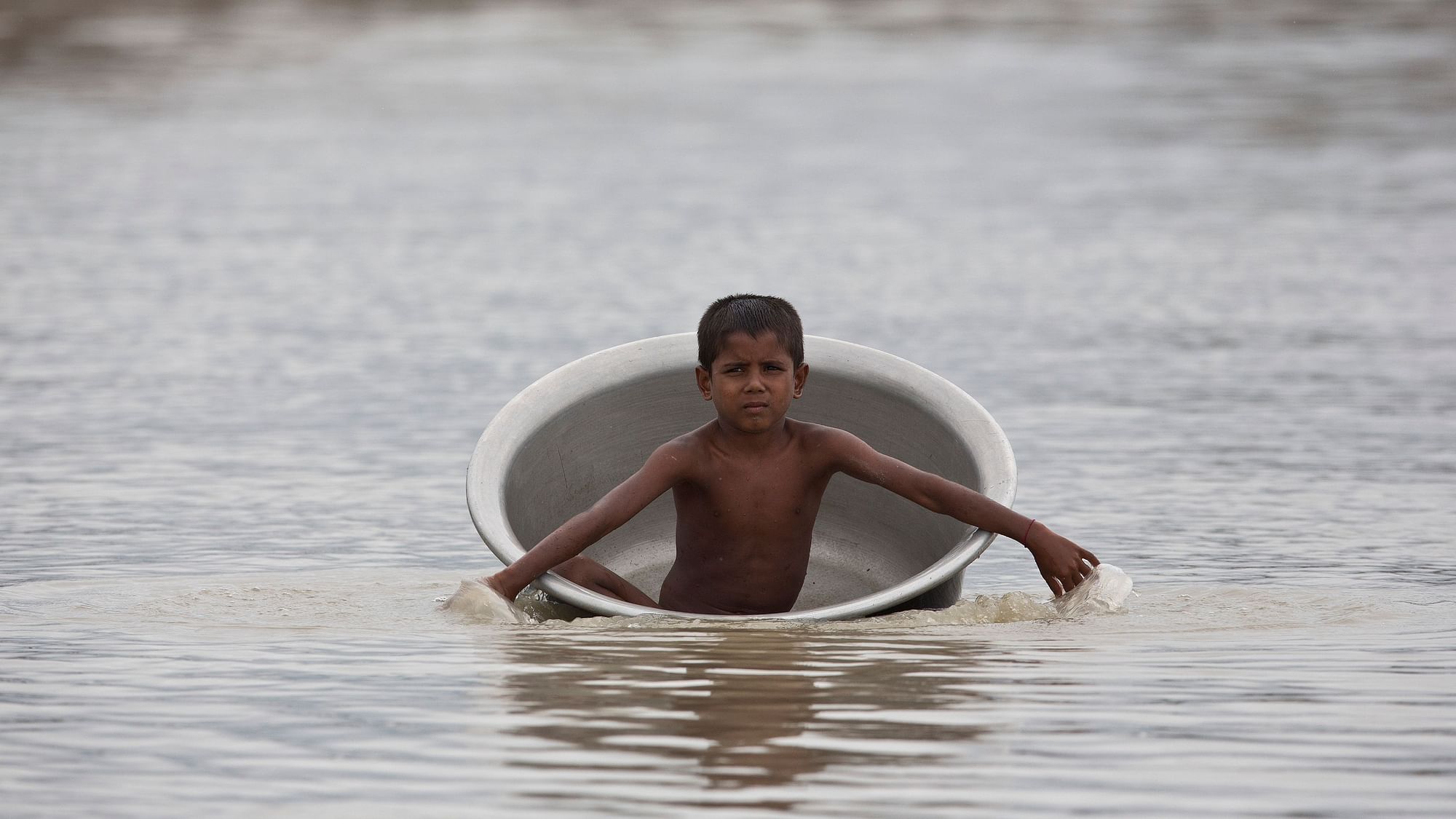 A flood affected boy floats in a container in Katahguri village along river Brahmaputra, east of Assam’s Guwahati, on Sunday, 14 July  2019.&nbsp;