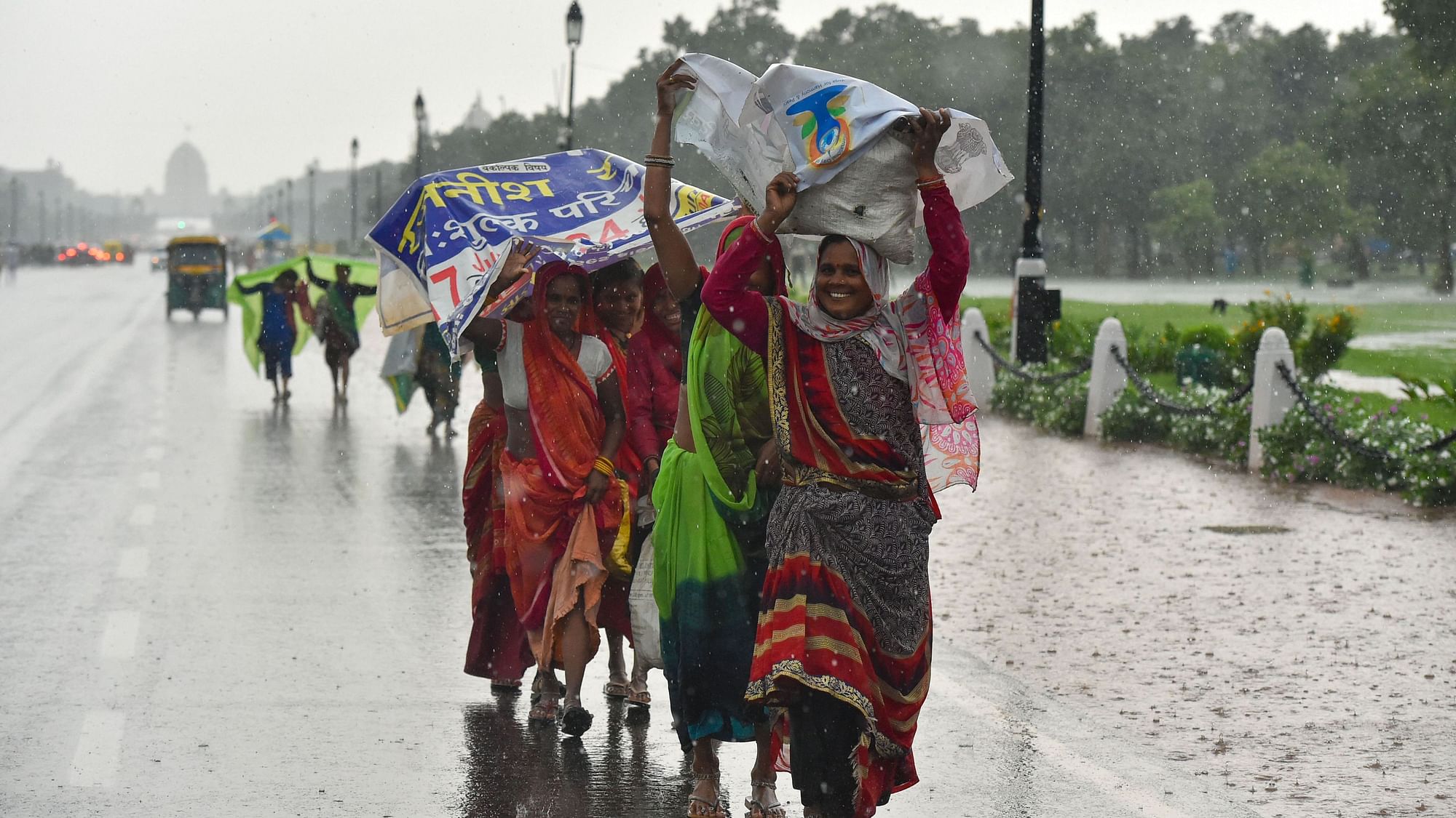 Women try to cover themselves with plastic banners as they walk along the Rajpath during rains, in New Delhi on Sunday, 21 July.