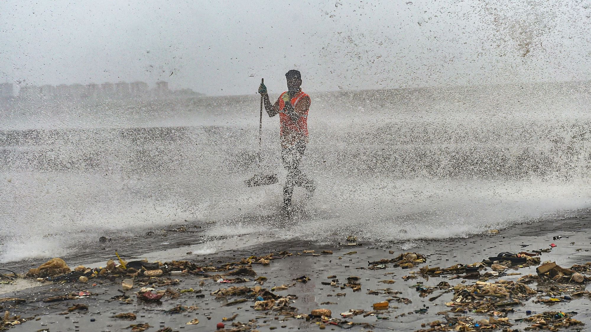 A civic worker clears the plastic waste and garbage thrown out of the sea during a high tide at Marine Drive promenade in Mumbai, on Sunday, 7 July.