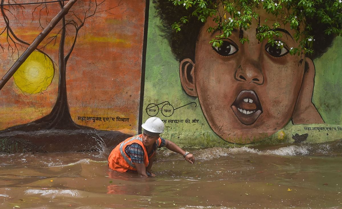 A Municipal worker cleans an open manhole on a waterlogged street following heavy monsoon rains