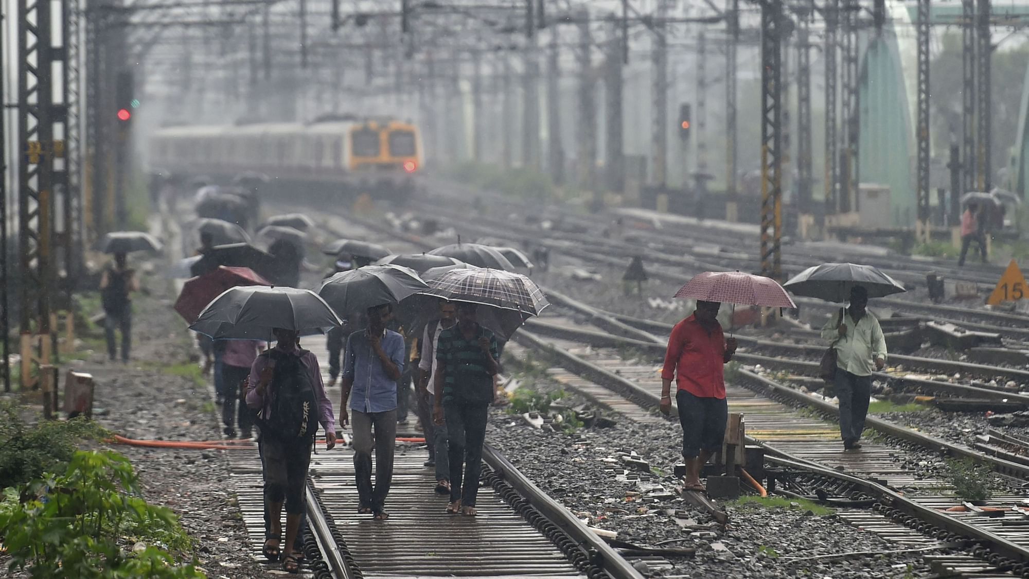 People walk on the railway tracks as heavy monsoon rains hit the central suburban trains service, in Mumbai, Tuesday, 2 July, 2019.