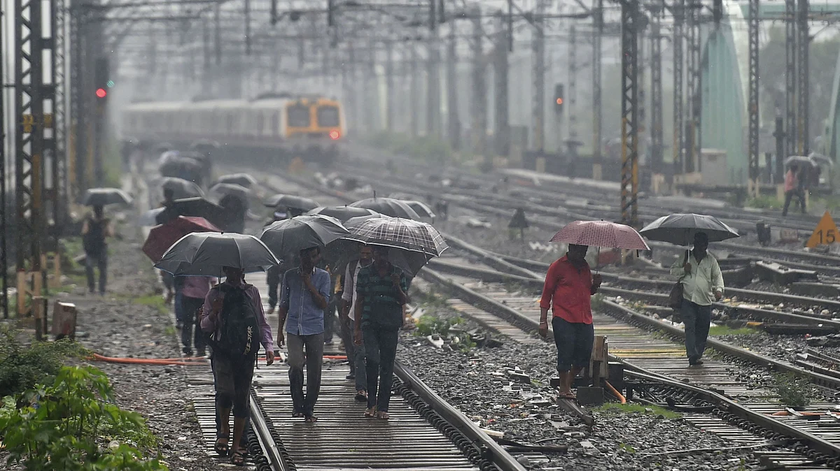 People walk on the railway tracks as heavy monsoon rains hit the central suburban trains service, in Mumbai, Tuesday, 2 July, 2019.