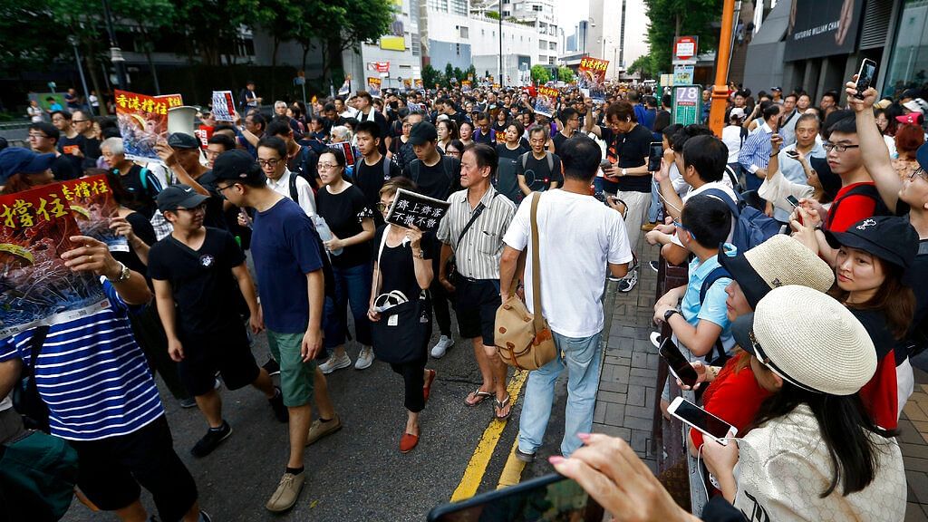 In this July 7, 2019, photo, mainland Chinese tourists, right, watch and film the protesters with placards march on a street in Hong Kong.