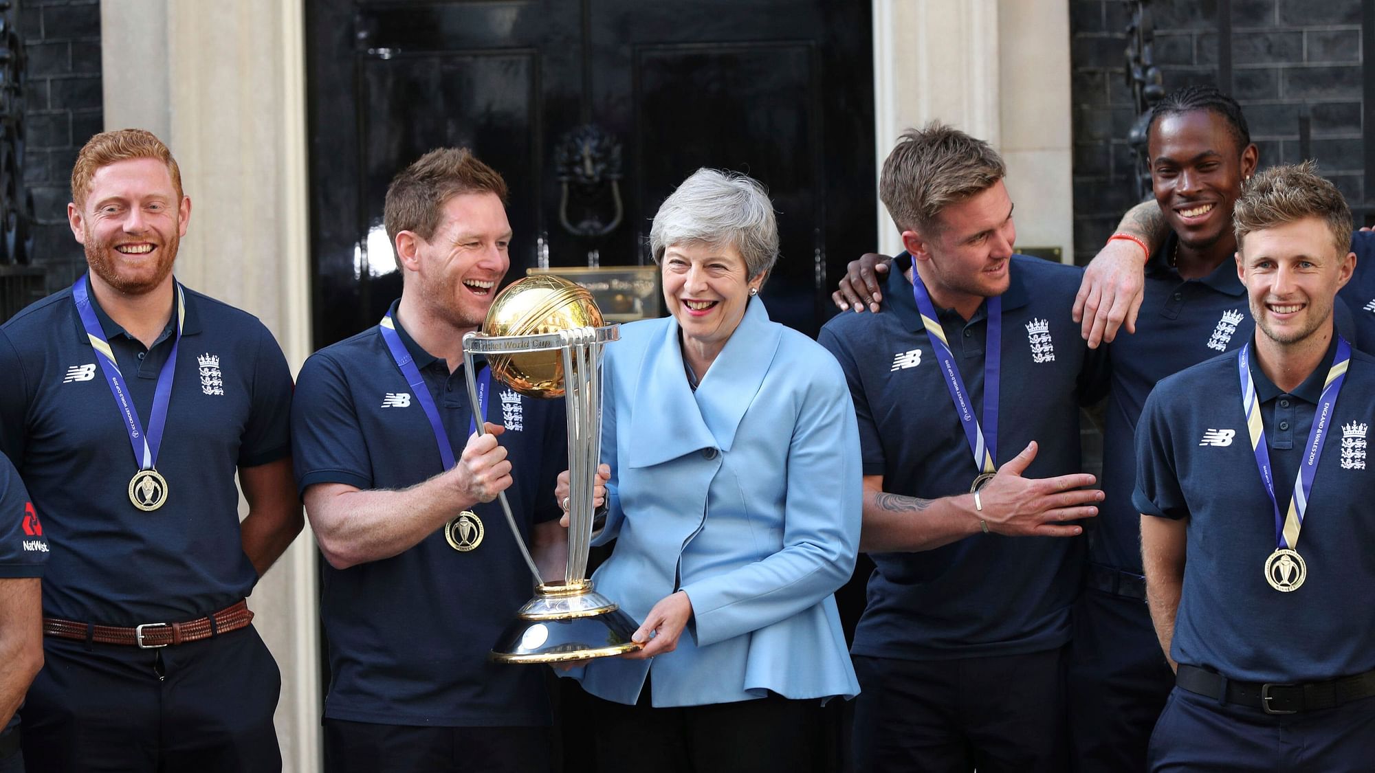Britain’s Prime Minister Theresa May smiles as she stands with England cricket captain Eoin Morgan, members of the team and the trophy after England won the Cricket World Cup, outside Downing Street in London, Monday, July 15, 2019. (Yui Mok/PA via AP)