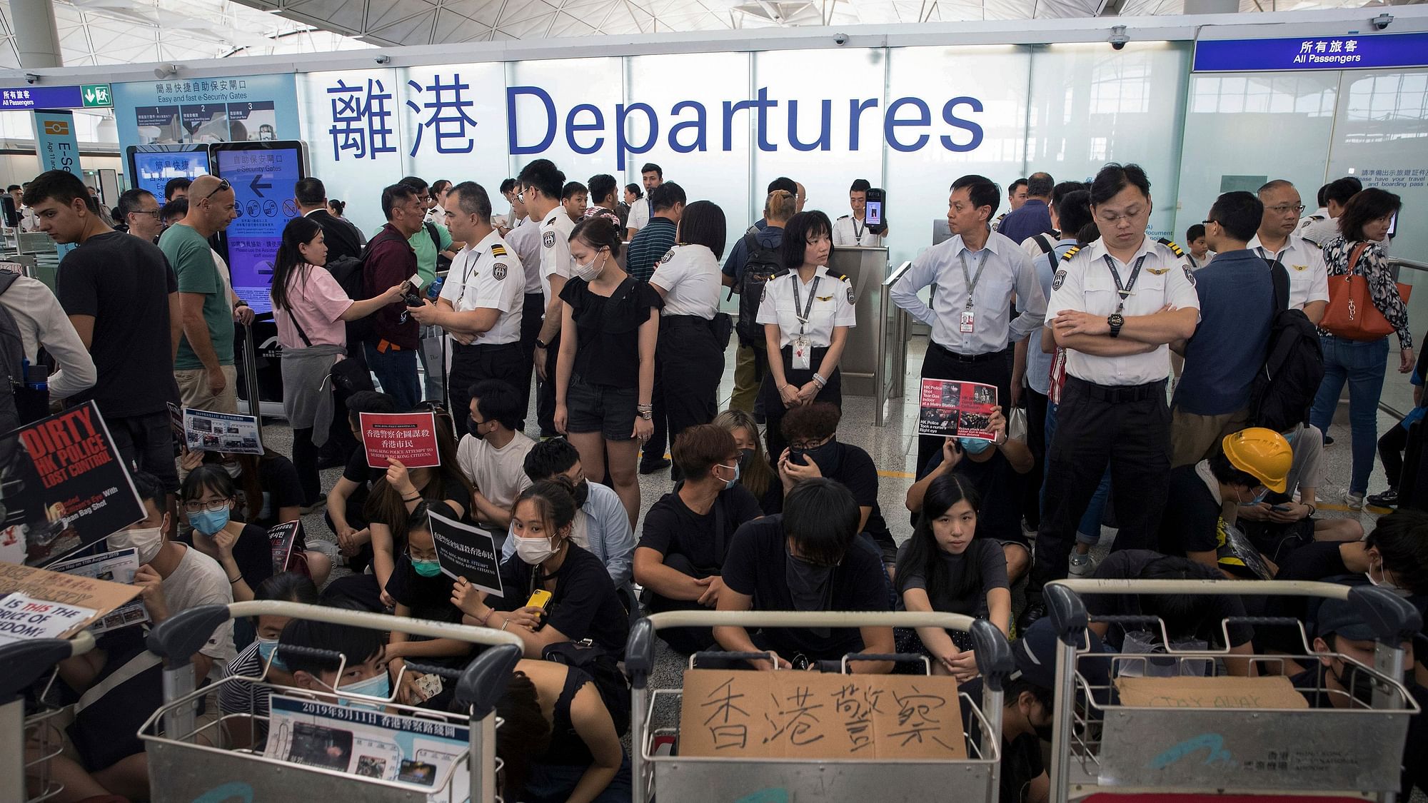 Airport security personnel stand guard as travellers walk past protesters holding a sit-in rally at the departure gate of the Hong Kong International Airport in Hong Kong, Tuesday.