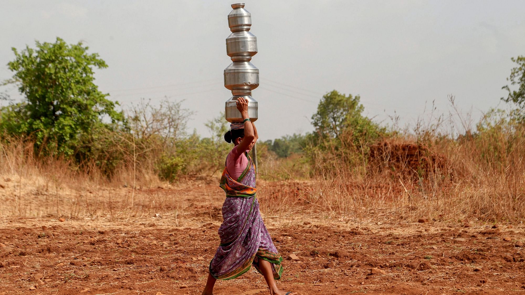  A woman carries multiple pots as she fetches water from a well, in Dhasai village of Thane district.