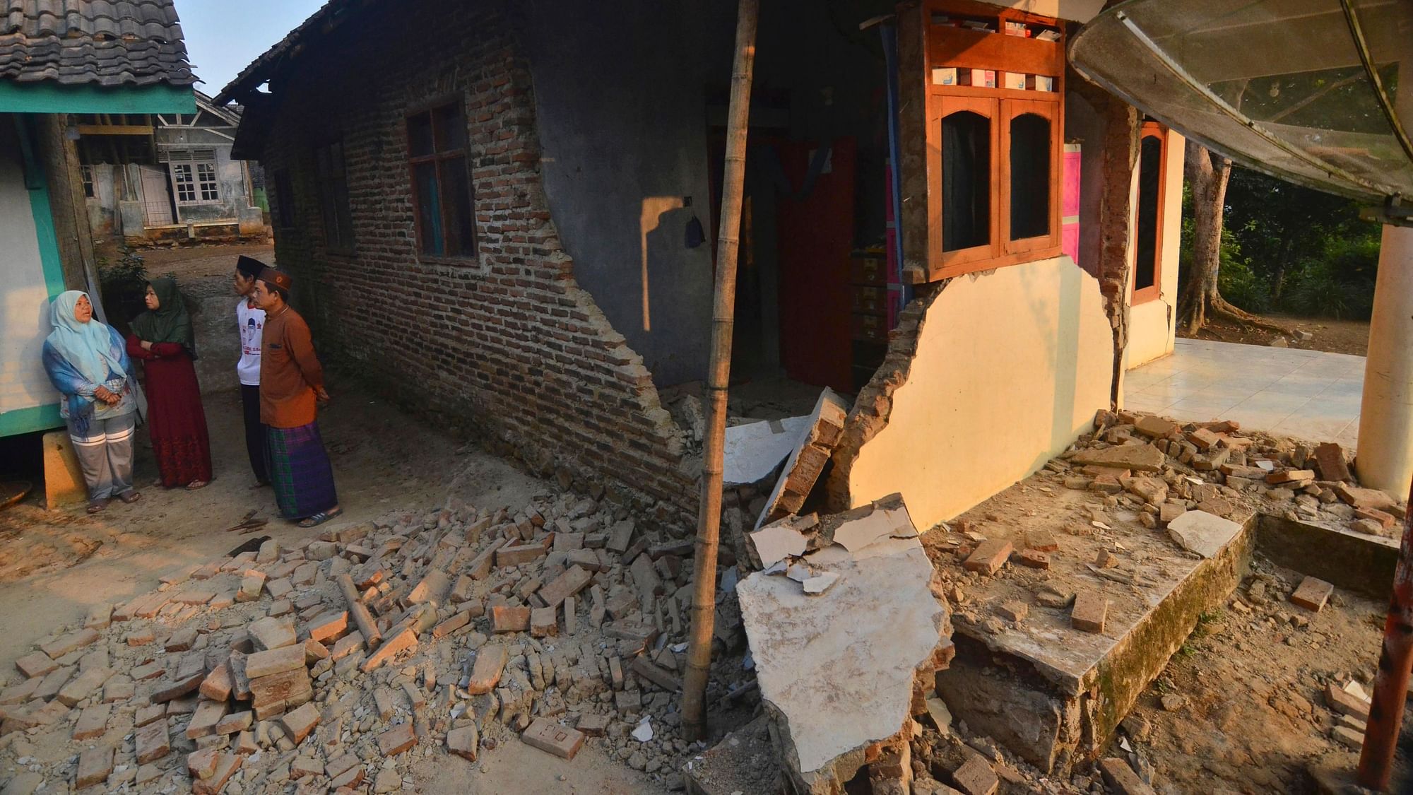 Residents talk near a house damaged in an earthquake in Mandalawangi, Banten province, Indonesia