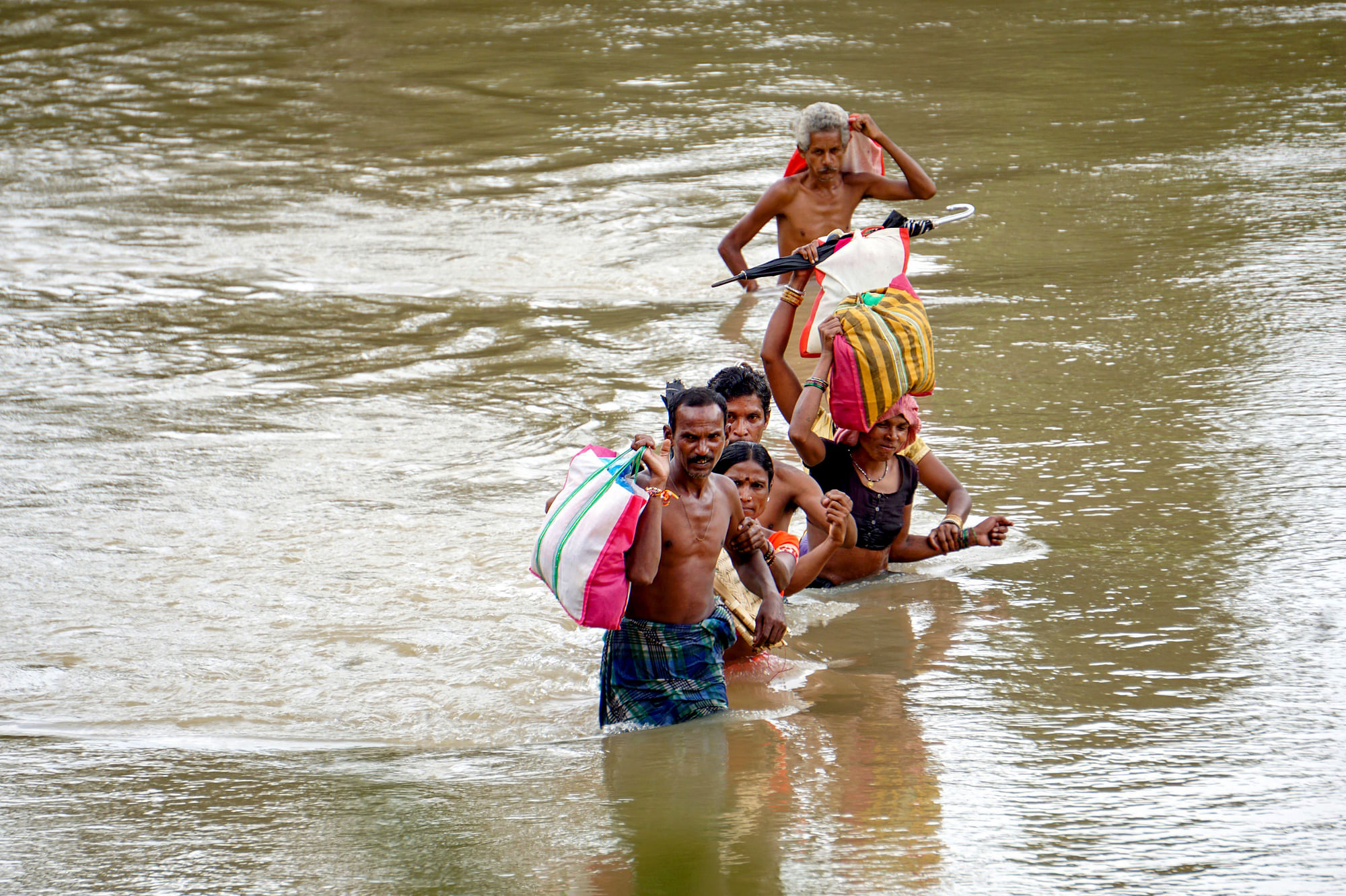 A group of people carrying their essentials wades through a flood-affected area following incessant rain, in Vijayawada