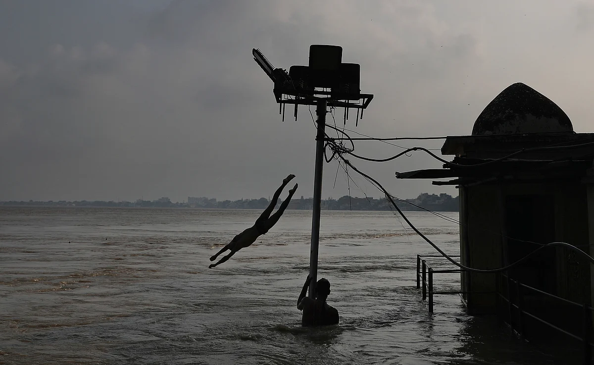 A boy jumps from the roof of a building into the waters of the swollen River Ganga as another boy holds onto a partially submerged electric pole in Varanasi, India, Sunday, 22 September.