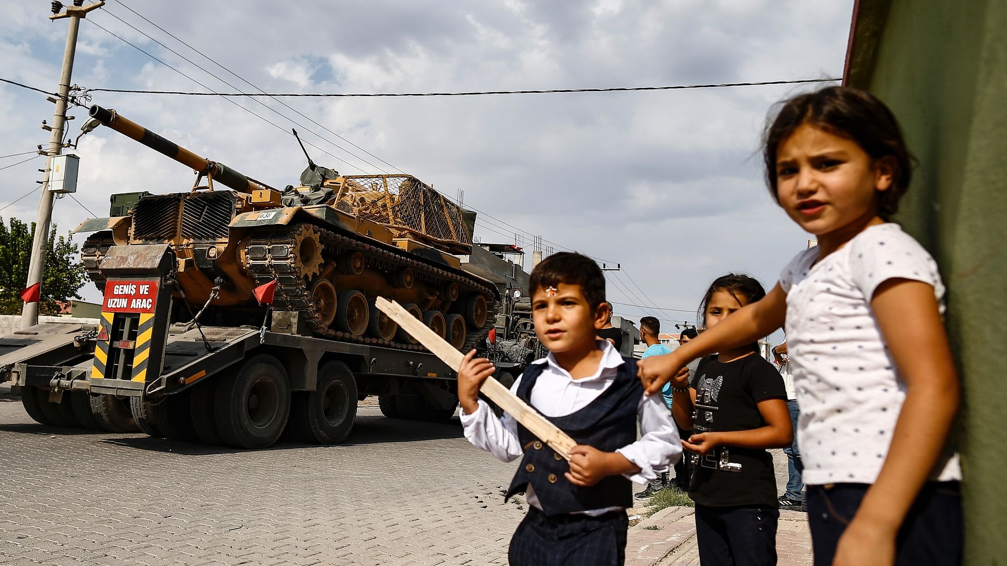 Children watch as Army tanks are transported on trucks in the outskirts of the town of Akcakale, in Sanliurfa province, southeastern Turkey, at he border of Syria.&nbsp;
