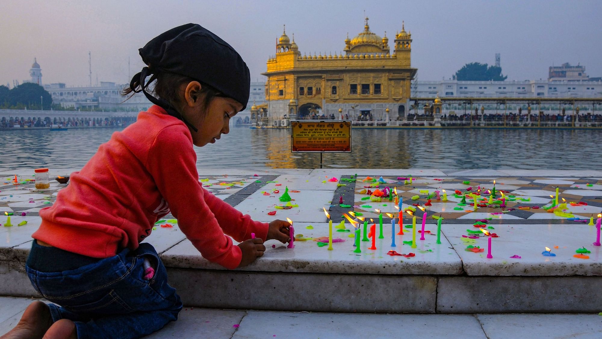 A young devotee lights a candle on the occasion of the 550th birth anniversary of Sikhism founder Guru Nanak Dev ji, in Amritsar.
