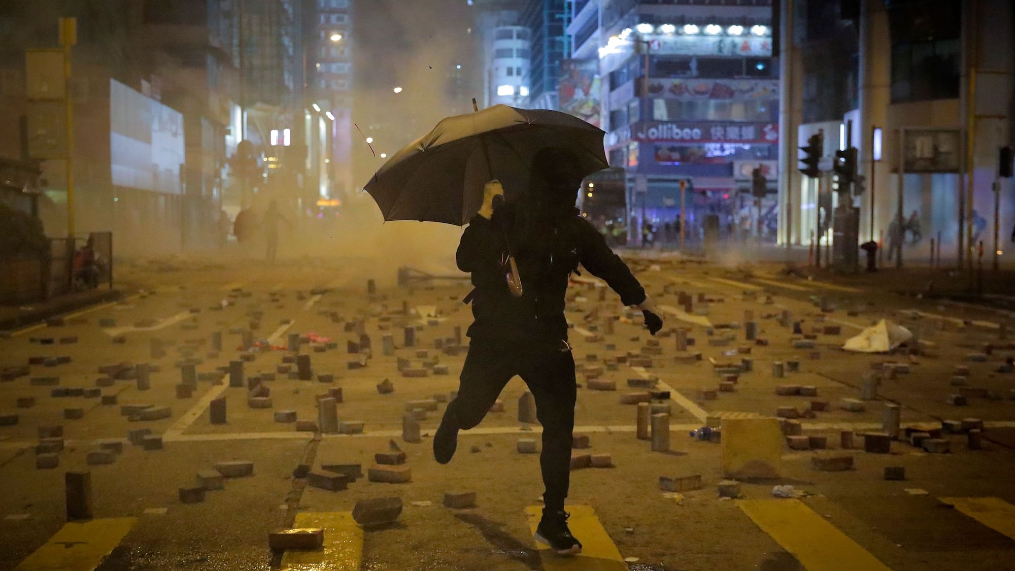 A protester with an umbrella runs away from tear gas fired by riot police on a street scattered with bricks during a protests in Hong Kong
