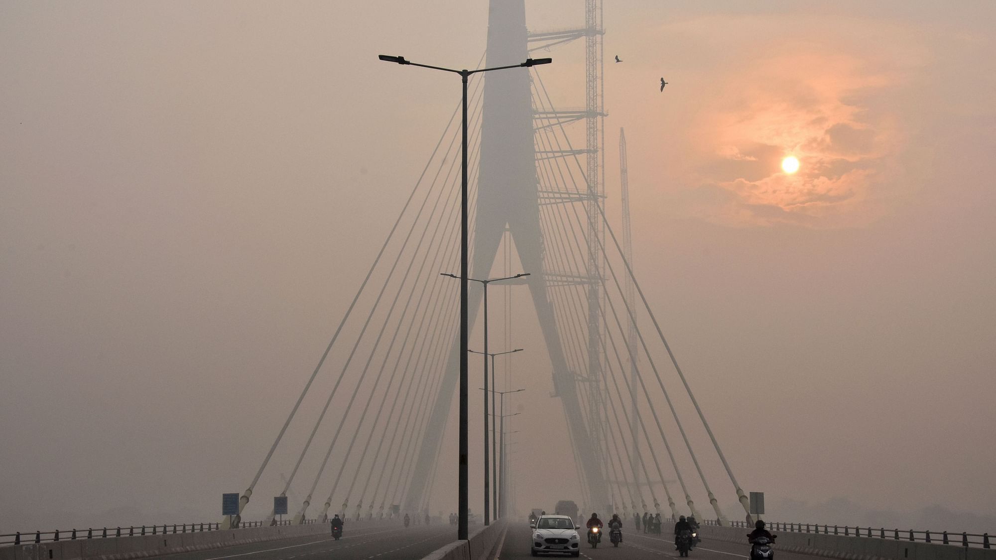 The sun is vaguely seen behind the Signature Bridge amid heavy smog, in New Delhi.
