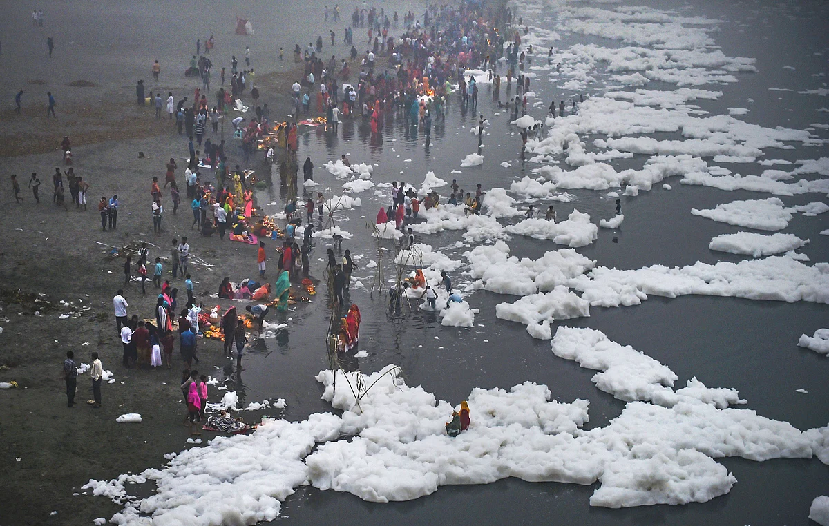 Devotees offers prayers to the rising sun as toxic foam floats on the surface of polluted Yamuna river during Chhath Puja celebrations, at Kalindi Kunj, in New Delhi on 3 November. 