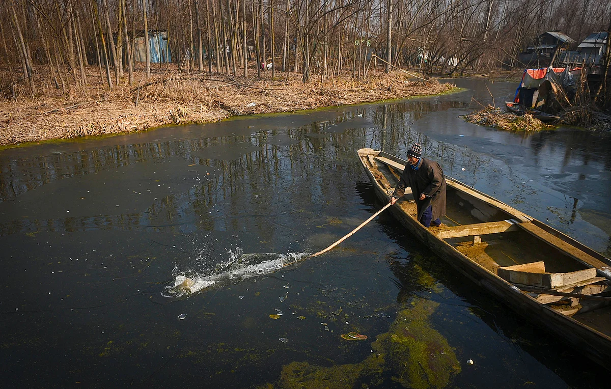 A man breaks the ice layer formed on the surface of the Dal Lake due severe cold, to make way for his boat in Srinagar on Friday, 27 December.