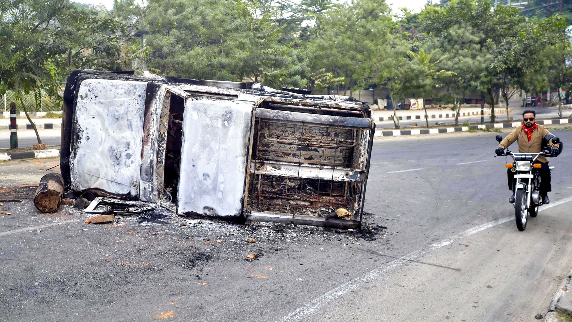 Man rides past a torched vehicle set on fire by anti-Citizenship Act protests in Guwahati.
