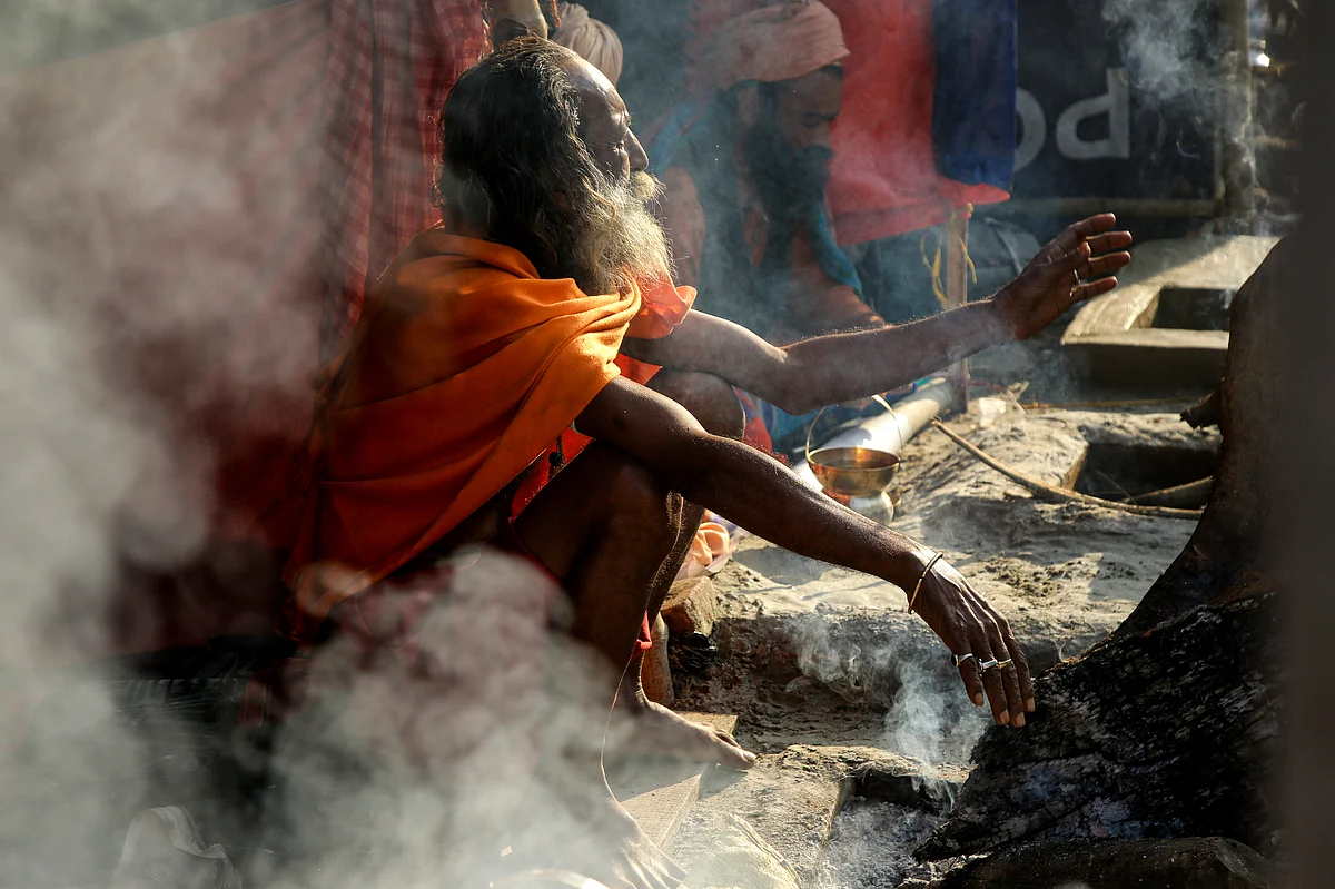 A monk headed to the Gangasagar pilgrimage tries to keep himself warm near a fireplace at a transit camp in Kolkata, on Monday, 6 January.